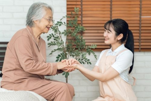 介護職員が高齢女性と手を合わせてコミュニケーションを取っている様子